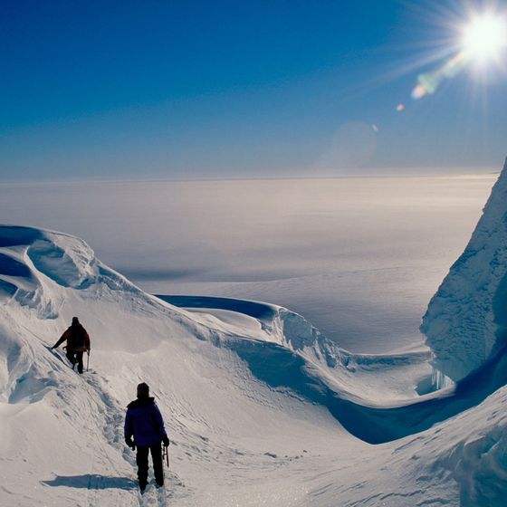 Two climbers descending a snow ridge under a bright sun